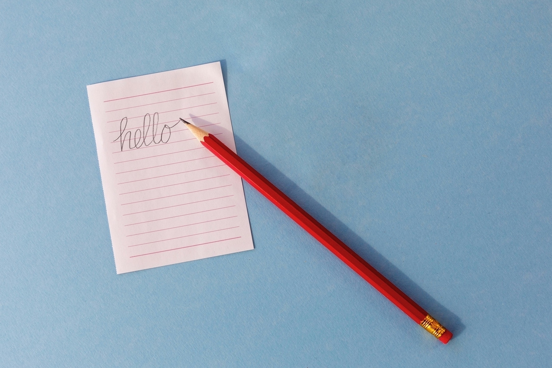 Red wooden pencil on a desk near a piece of paper with 'Hello' written on it