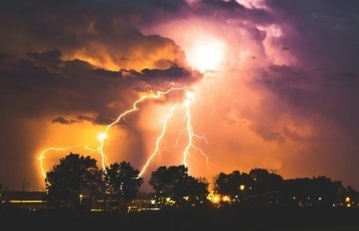 Storm clouds at night with lightning in the distance behind some trees